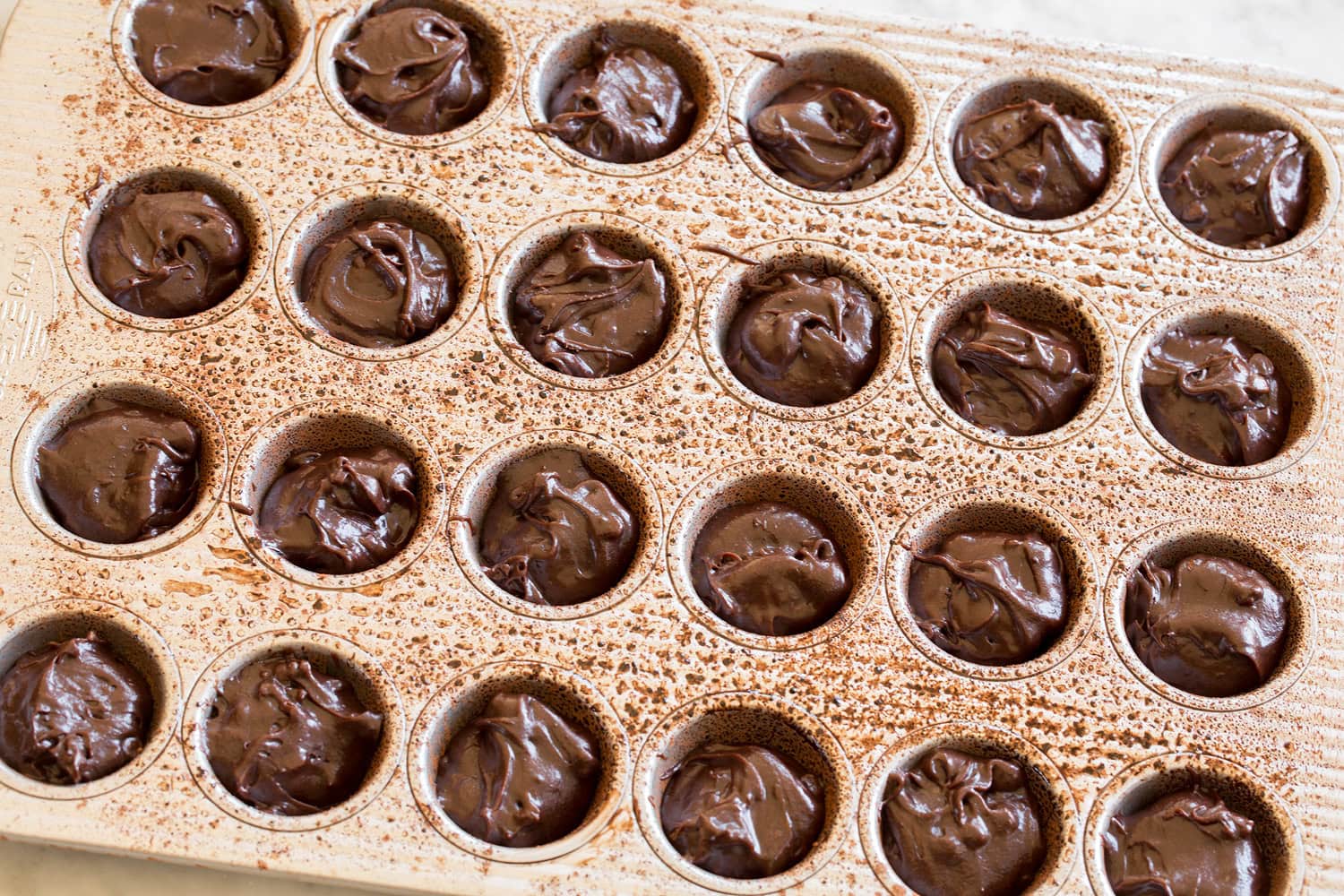Brownie batter added to mini muffin pan wells.